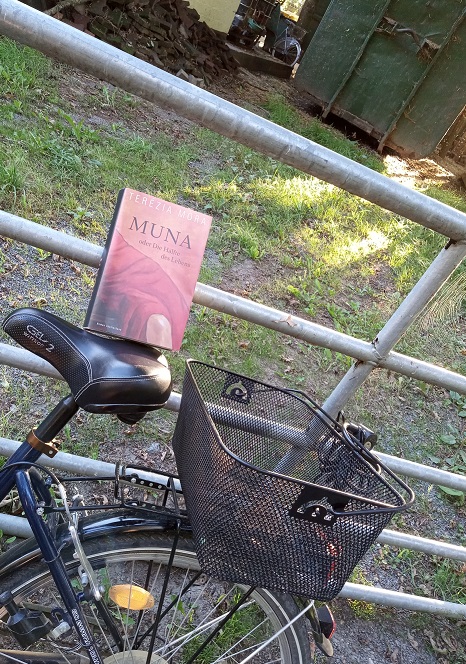 Das Buch steht auf einem Fahrradsattel und lehnt an einem Gitterzaun. Im Hintergrund ist ein alter Container und ein weiteres Fahrrad zu sehen.
Heute erzähle ich von einem Roman, der mich nachhaltig bewegt hat. Die Geschichte einer Frau und ihrer großen Liebe. Muna Roman Rezension Luchterhand