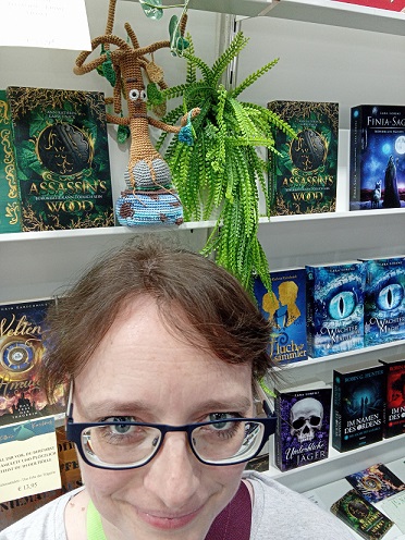 Wurzel sitzt zwischen Büchern im Regal, ich stehe davor und schaue in die Kamera